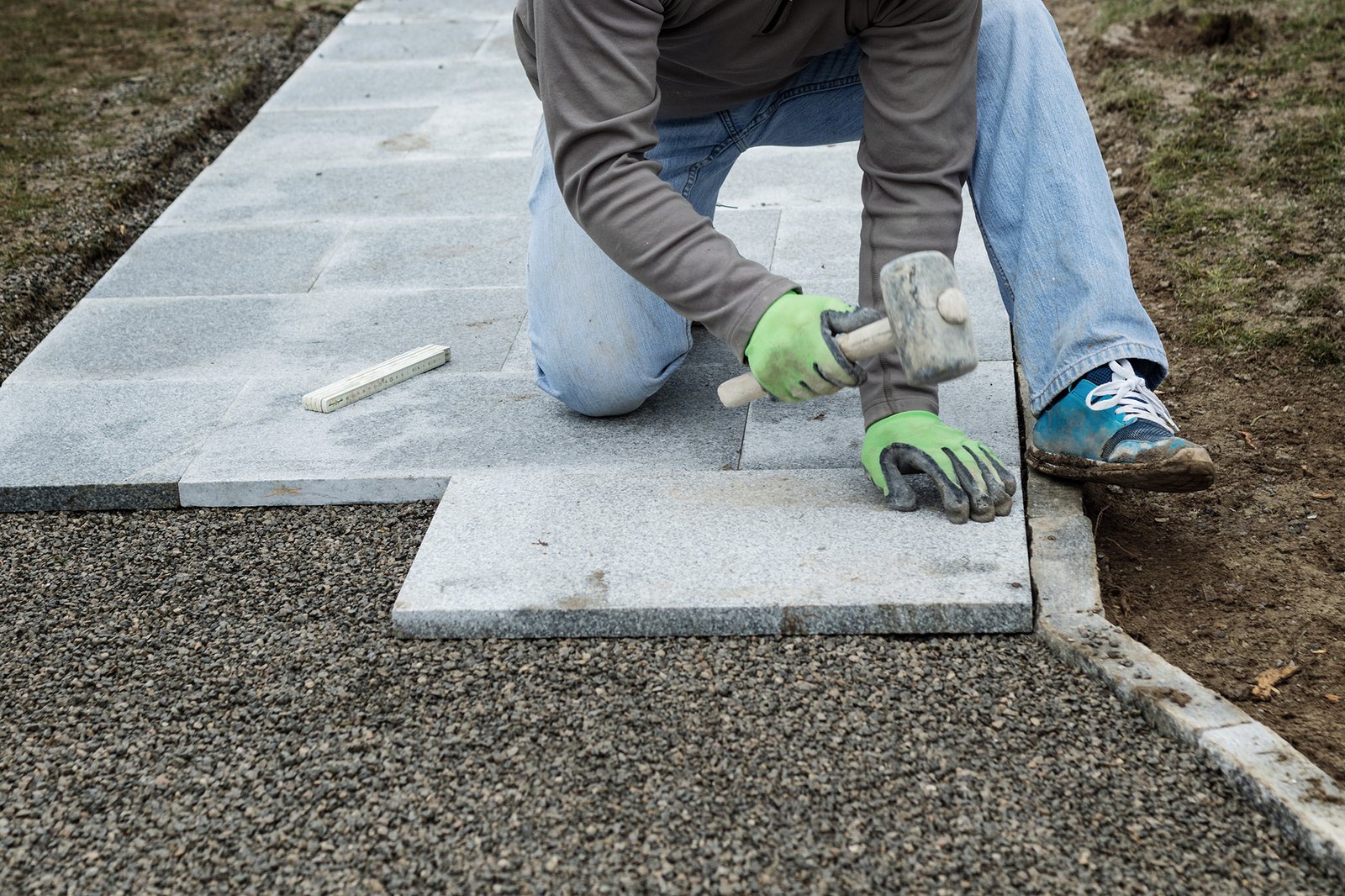 worker hammering the stone plates to install footpath at garden